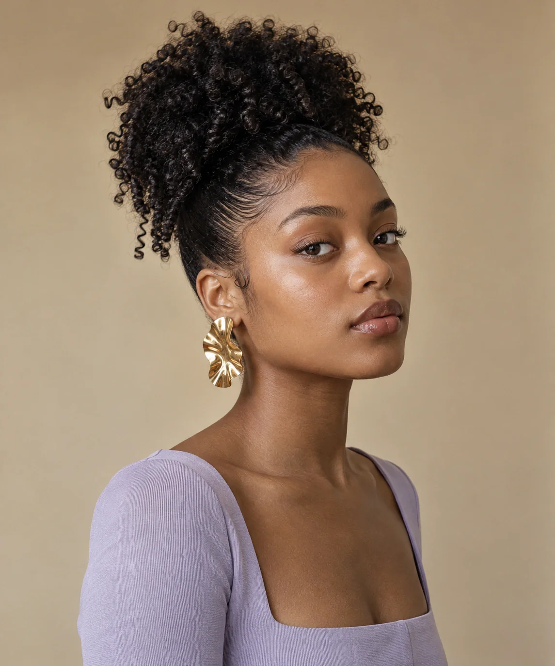 A young woman with a high natural-curl puff, a sculptural gold earring and a lavender square-neck top.